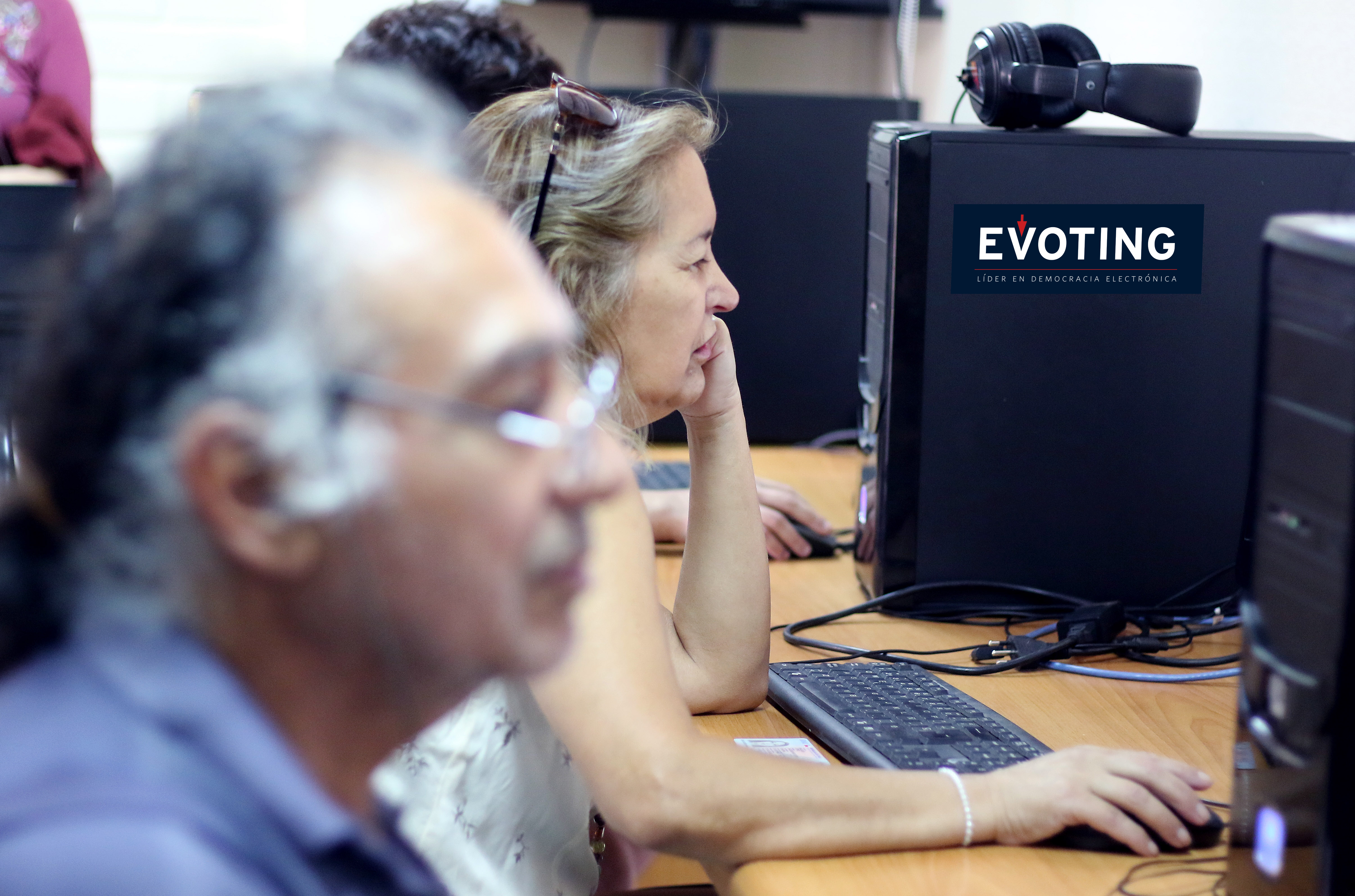 Dos ancianos votando con la plataforma de votación electrónica de EVoting, en un computador estacionario.